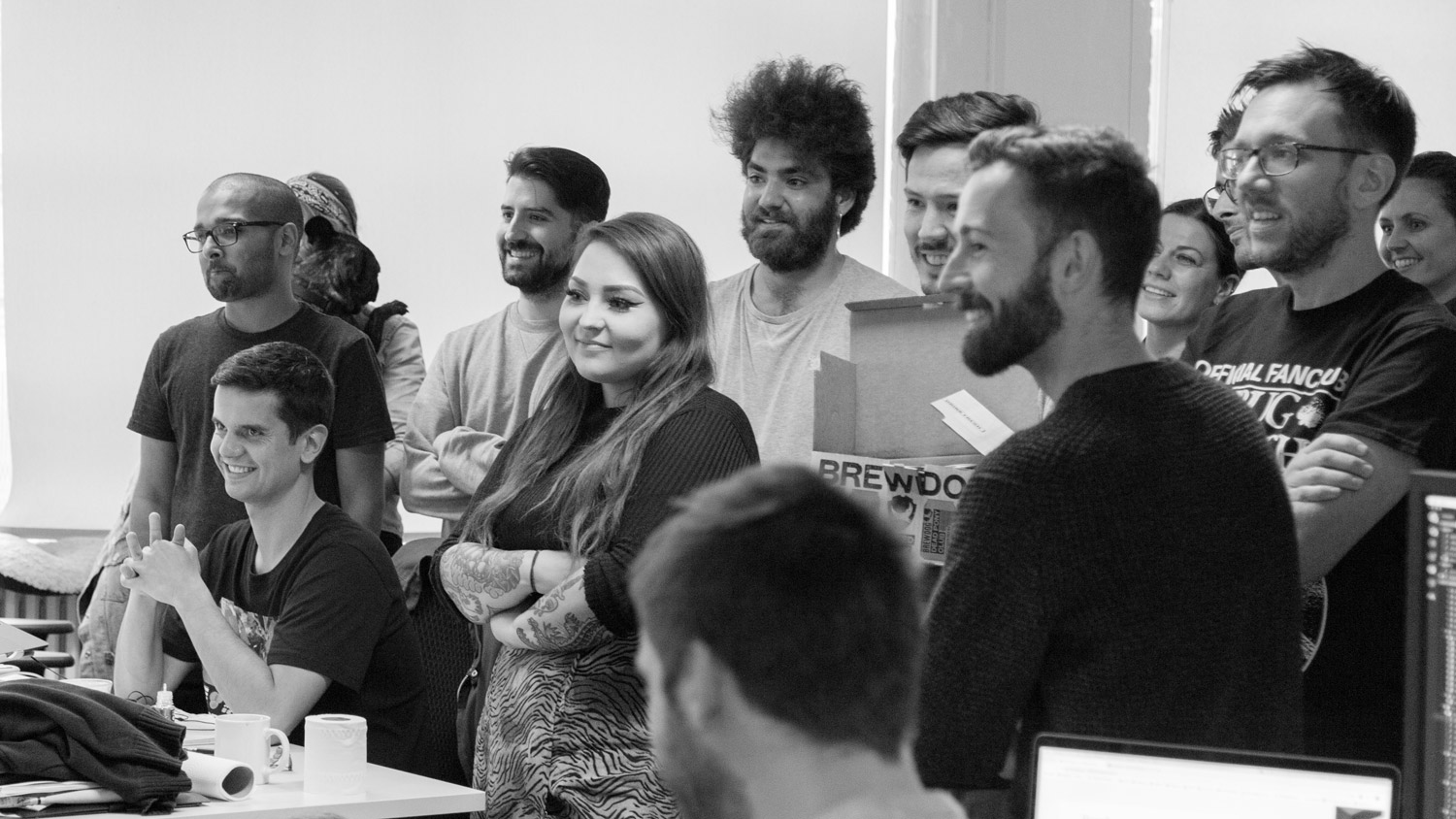 Large group of smiling colleagues in an office looking at someone speaking